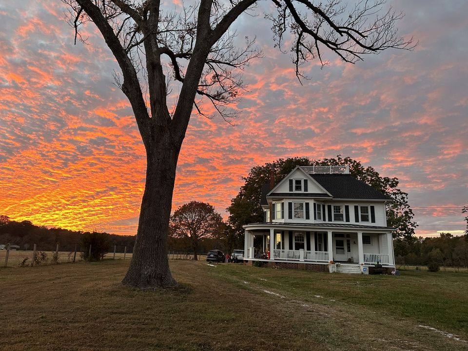 The Salt + Arrow Ranch farmhouse under an orange sunset sky
